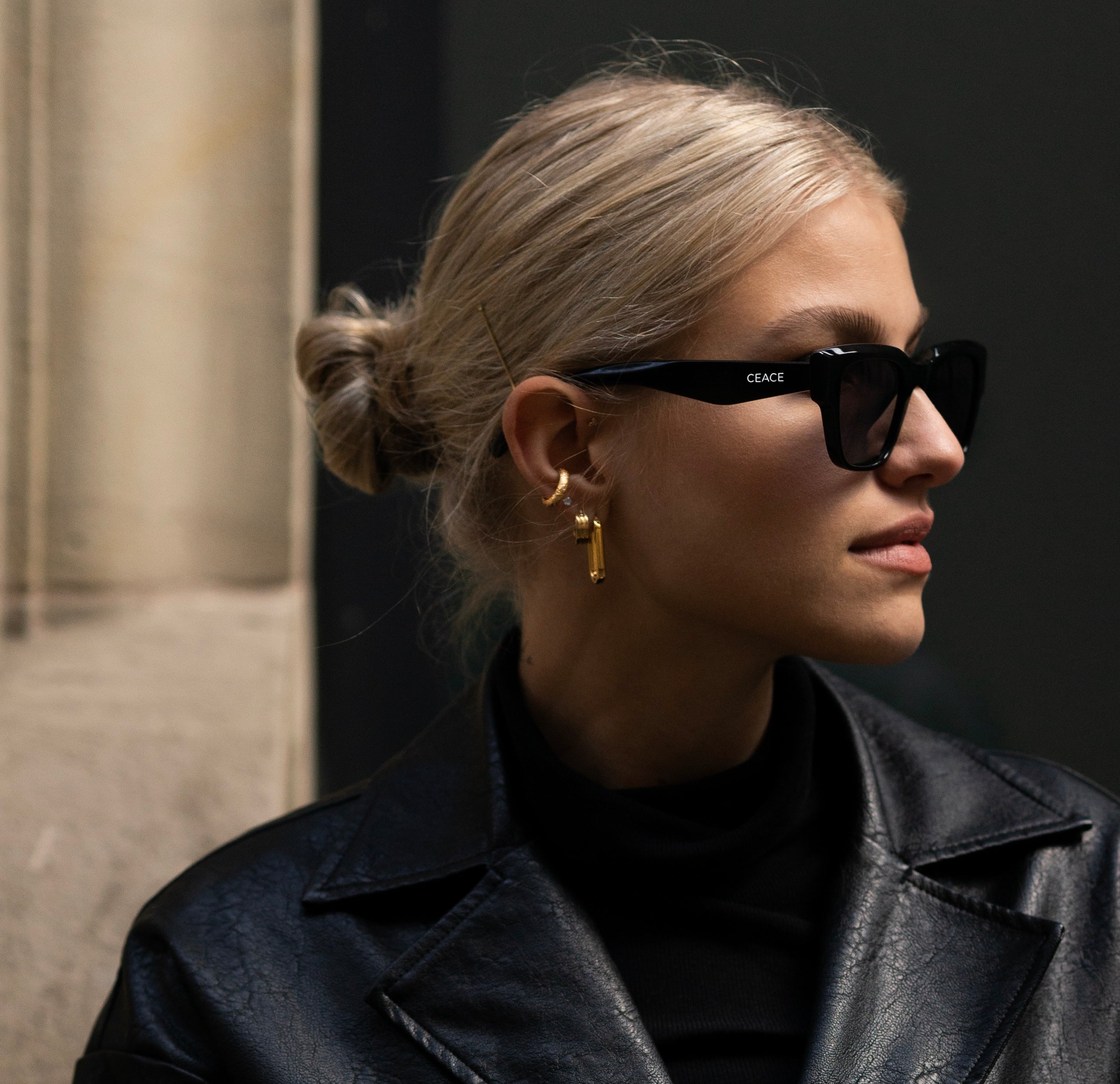 Das Bild zeigt eine Frau von der Seite in einem komplett schwarzen Outfit, ergänzt durch eine schwarze CEACE Sonnenbrille